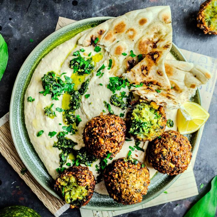 Wild garlic falafel on a plate of hummus with naan and lemon, on a black photography background.