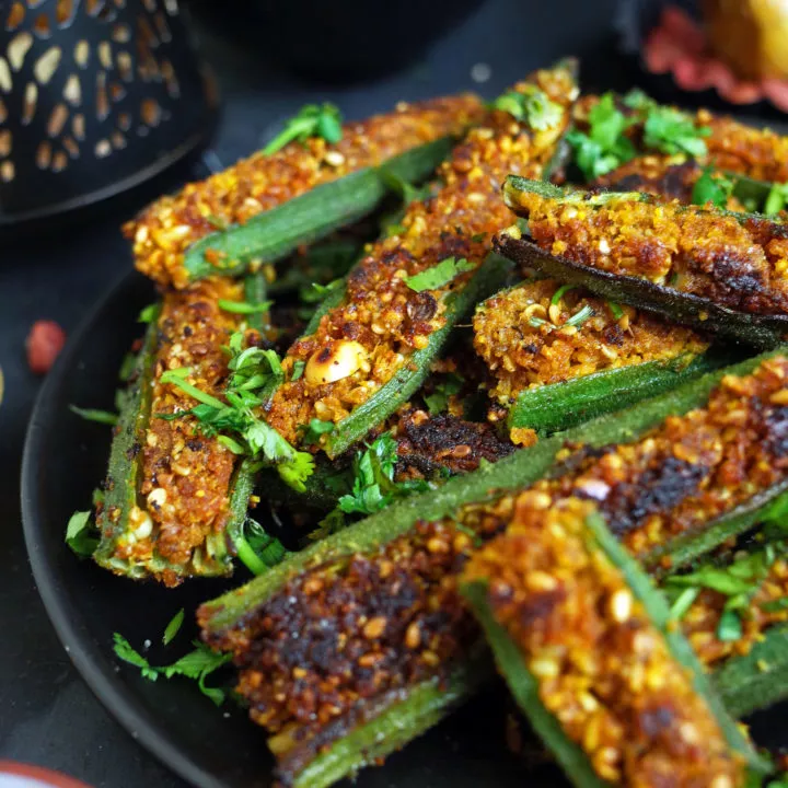 Maharashtrian Stuffed Bharli Bhindi on a black plate with Varan Dal in the background