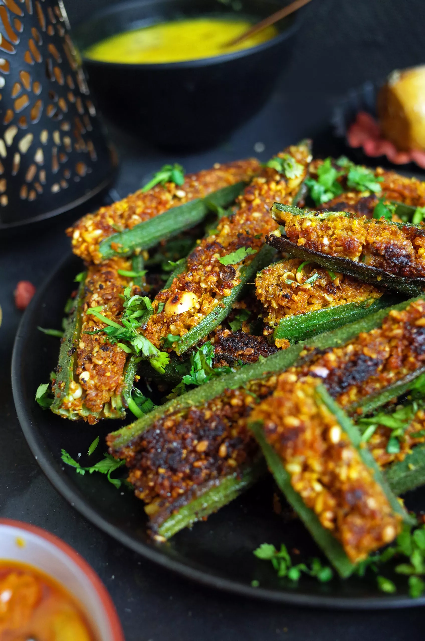 Maharashtrian Stuffed Bharli Bhindi on a black plate with Varan Dal in the background