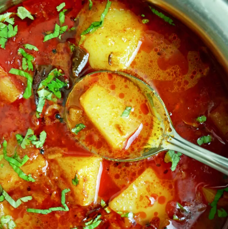 A silver spoon showing Maharashtrian Red Batata Rassa / Potato Curry topped with fresh Coriander.