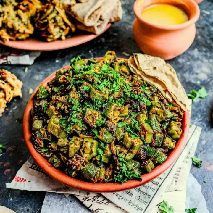 Bhindi masala okra curry in a clay bowl with dal, pakora, and roti.