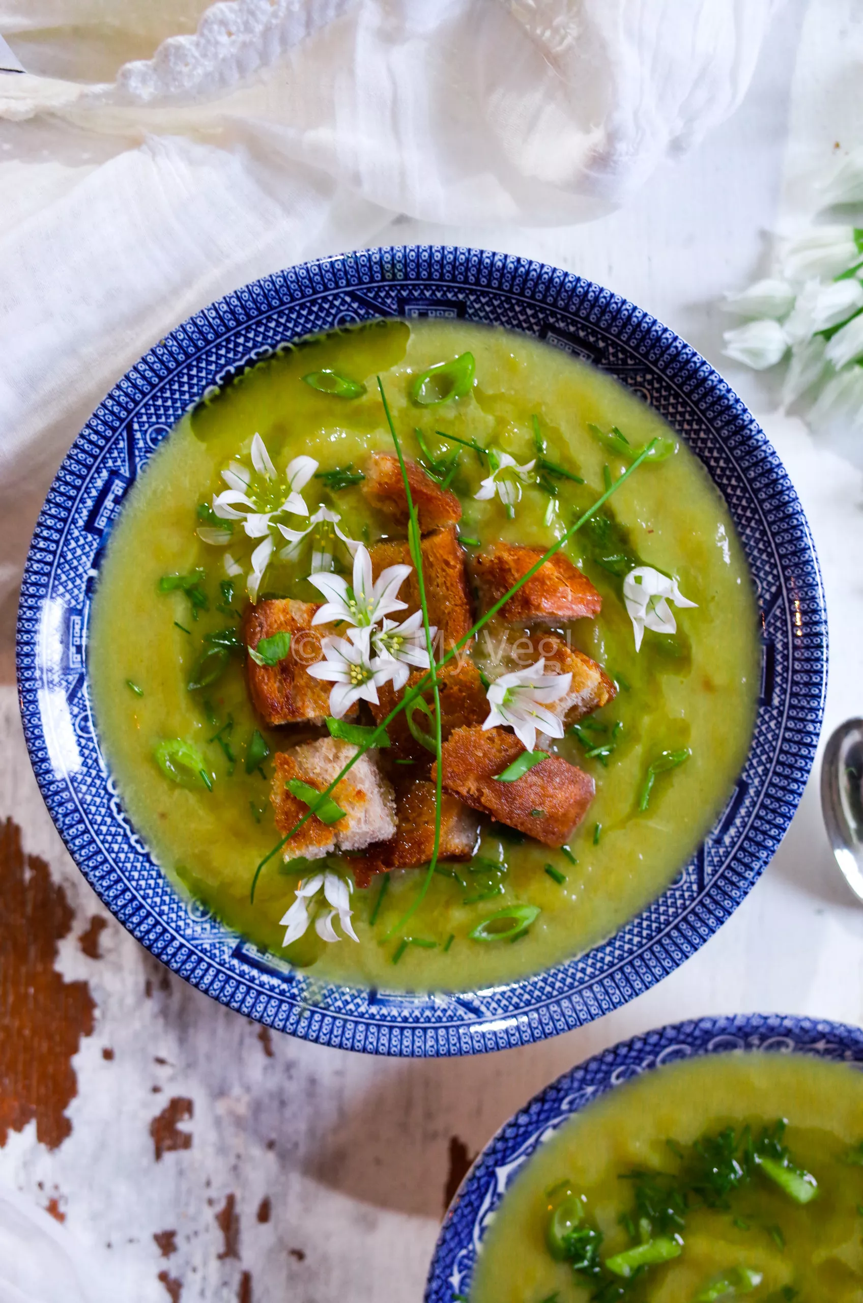 Vegan Leek Soup with Three Cornered Leek Oil, Croutons, and edible flowers in a blue bowl