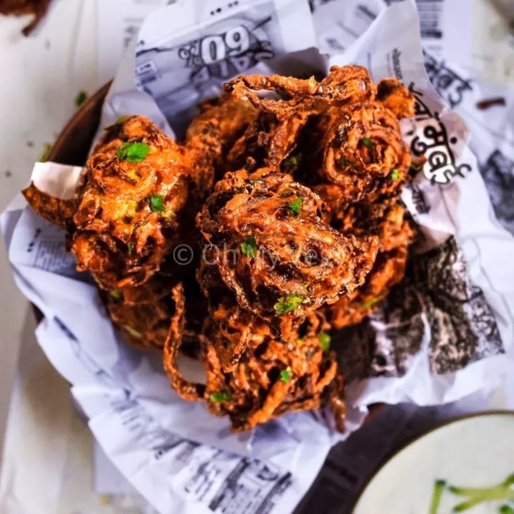 A pile of onion bhajis on newspaper with yoghurt raita on the side