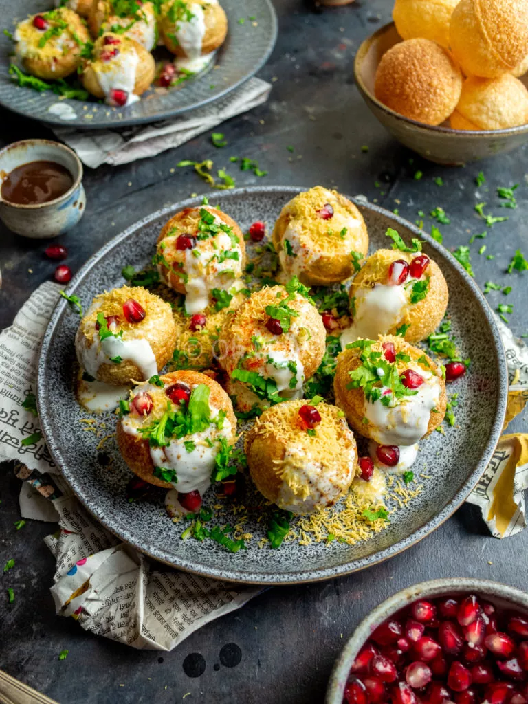 Dahi puri chaat bombs on a grey plate with newspaper and pomegranate on the background.