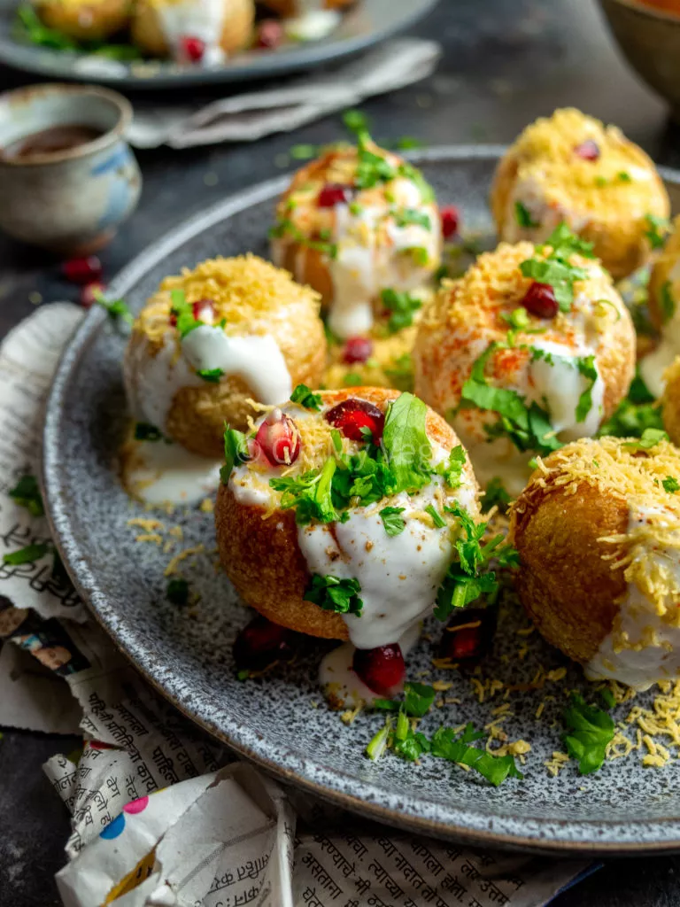 Close up photo of dahi puri chaat bombs on a grey plate with newspaper.