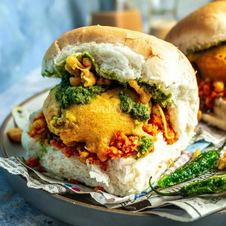 Vada pav on a blue background alongside fried green chilis.
