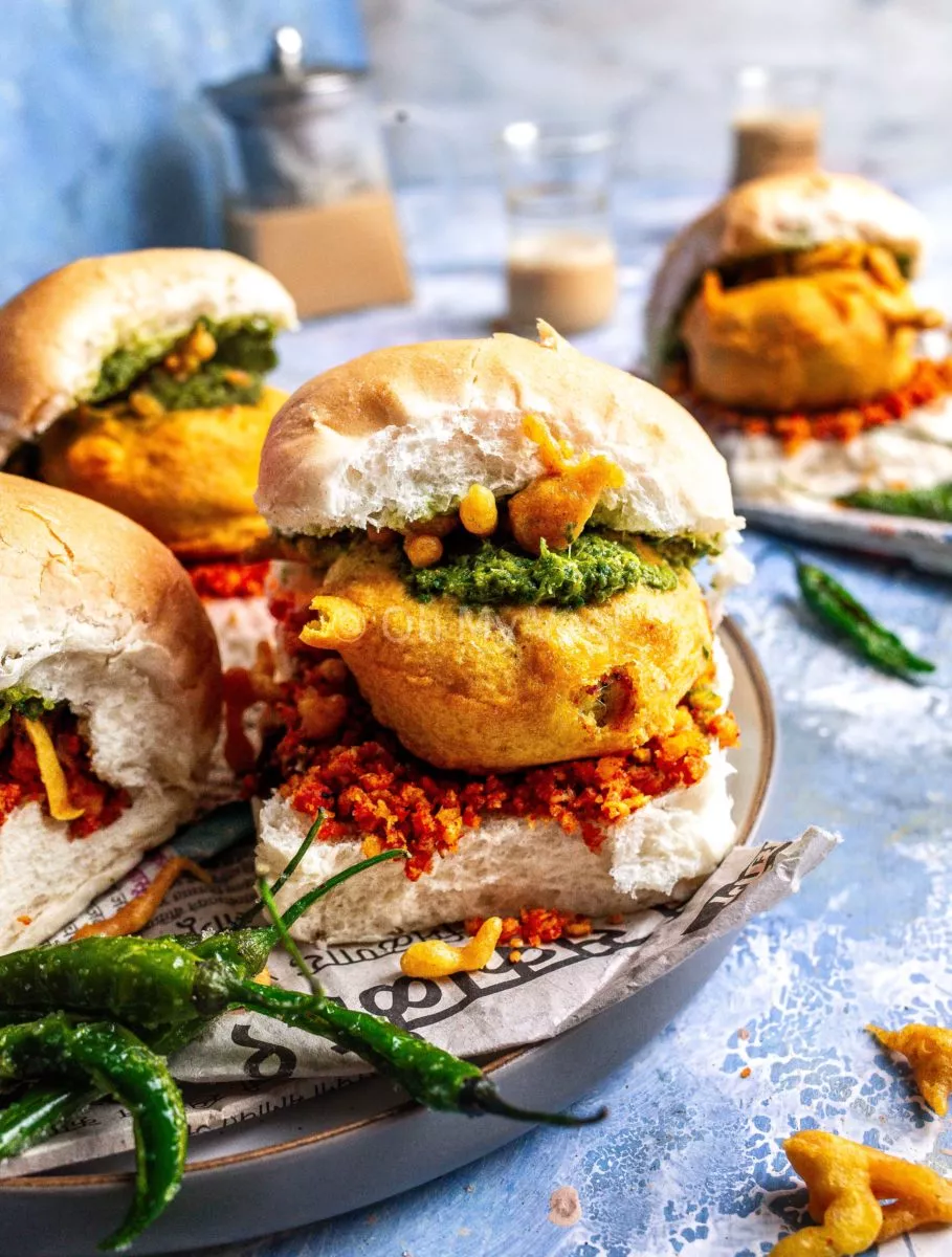 Vada pav on a blue background alongside fried green chilis. 