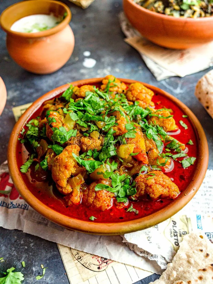 Maharashtrian Flower Batata Rassa in a clay bowl with raita in the background.