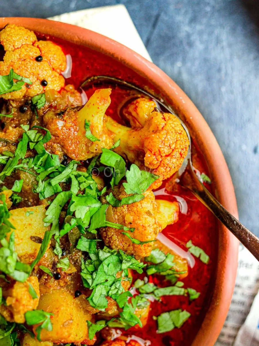 Close up photo of Maharashtrian flower batata rassa, or potato and cauliflower curry, in a clay bowl. It is topped with coriander.
