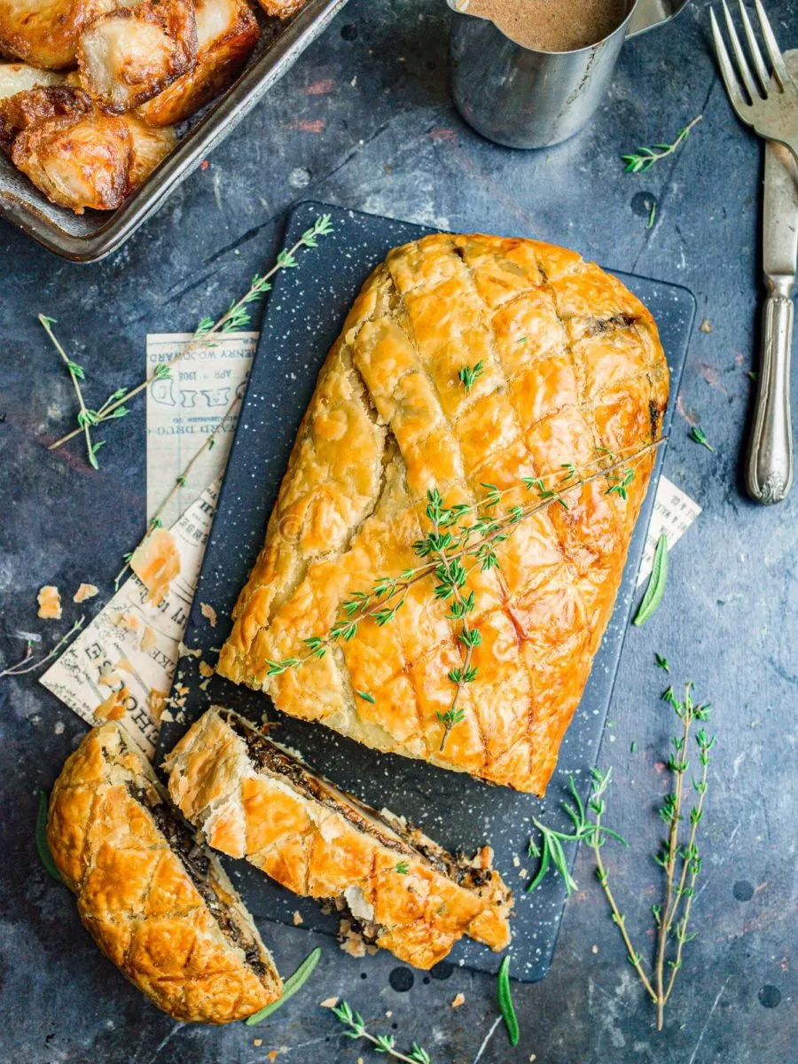 Vegan mushroom wellington with two slices cut out, on a food board with fresh thyme.