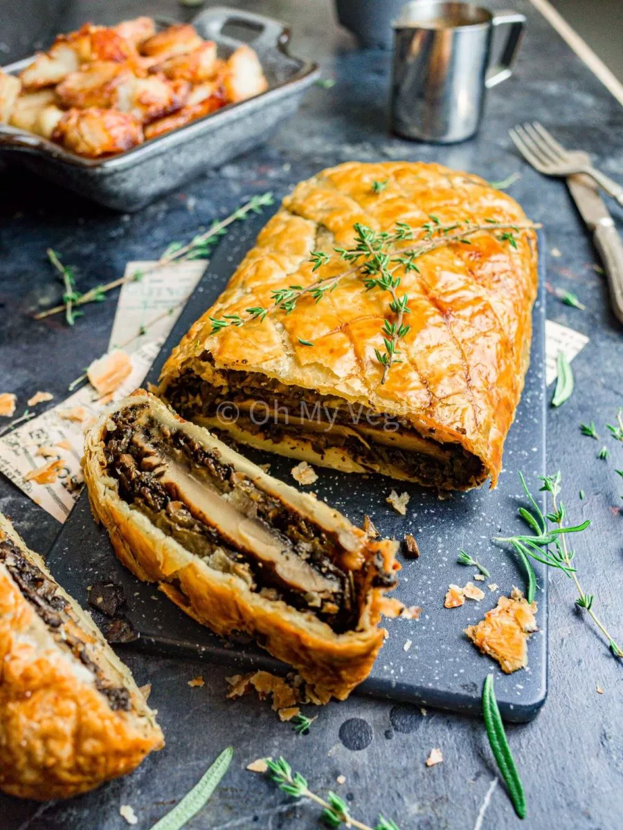 Vegan mushroom wellington topped with thyme, on a food board.