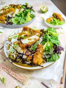 Two plates of vegan katsu curry with tofu and salad.