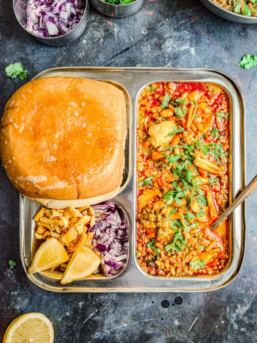 A steel plate with Maharashtrian misal pav, lemon slices, farsan, and kanda.