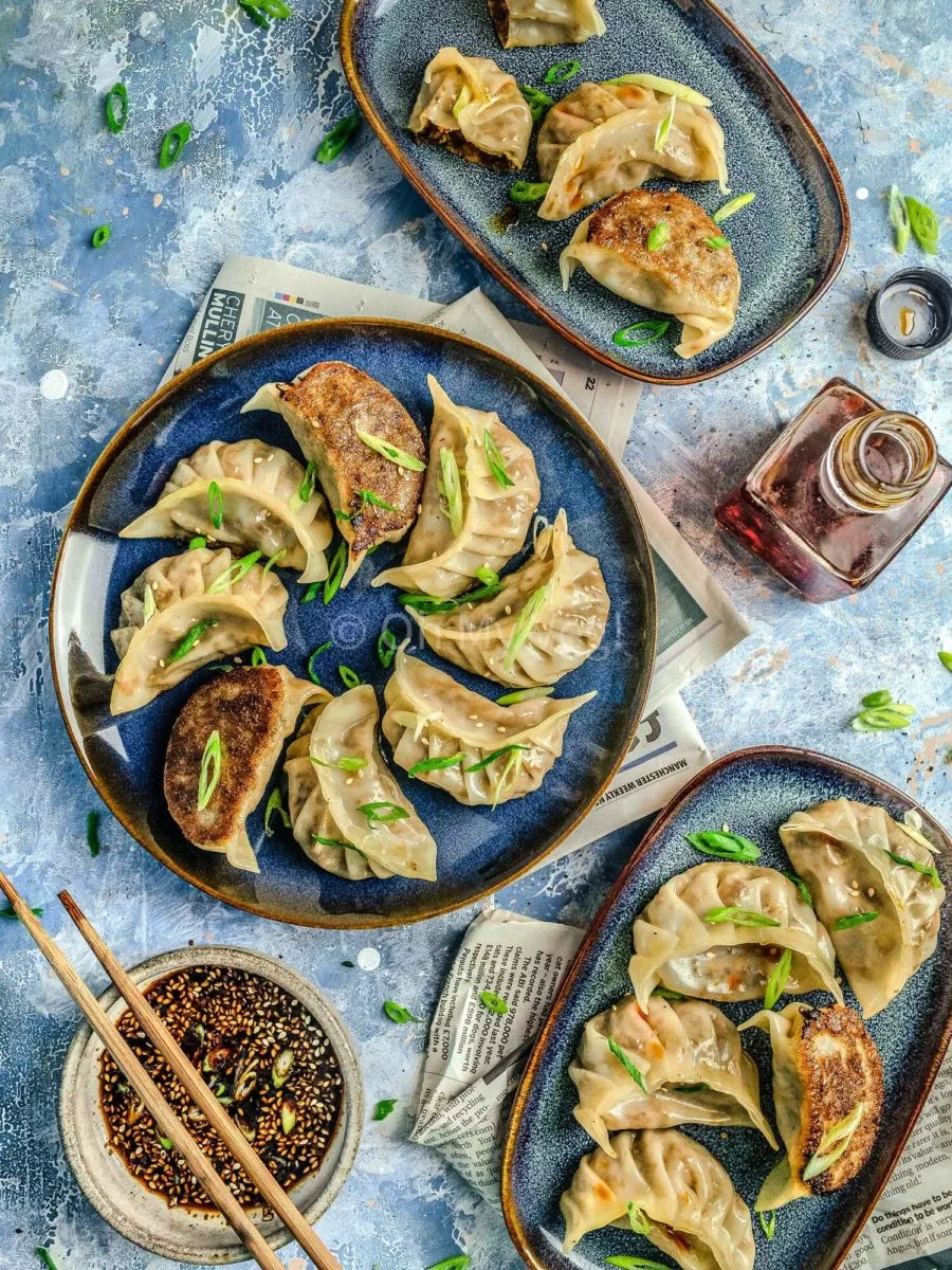 Vegetable gyozas on three blue plates with dumpling dipping sauce. 