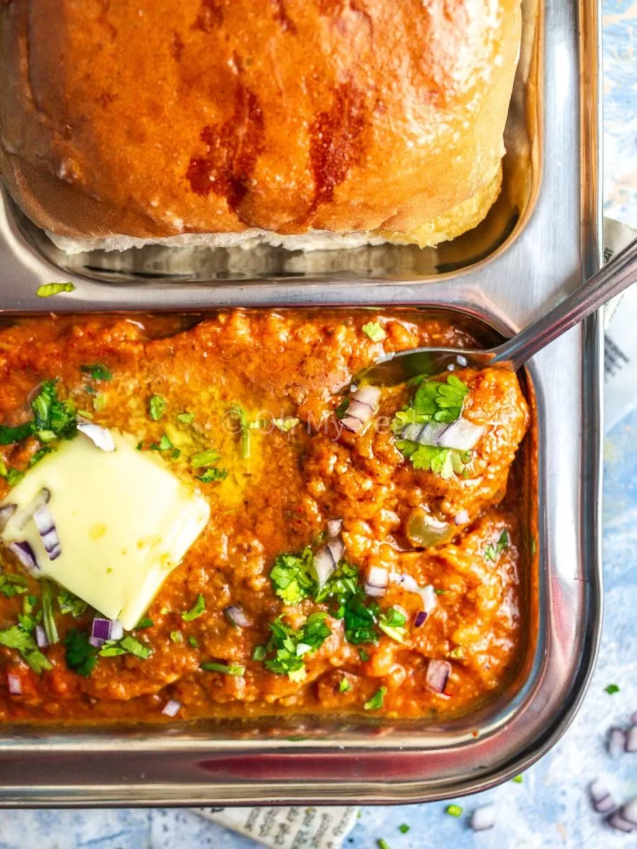 Spoon scooping out pav bhaji from a metal tray.