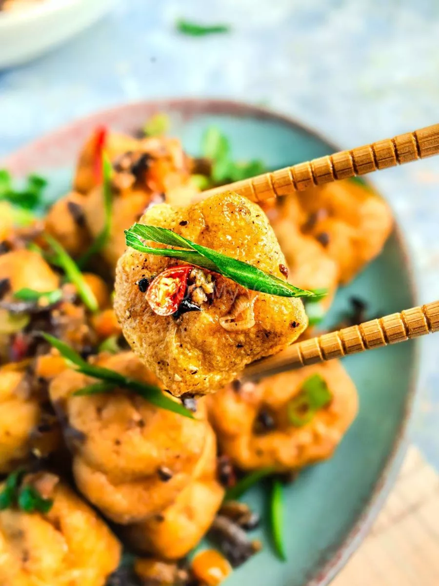 Chopsticks holding tofu with chilies..