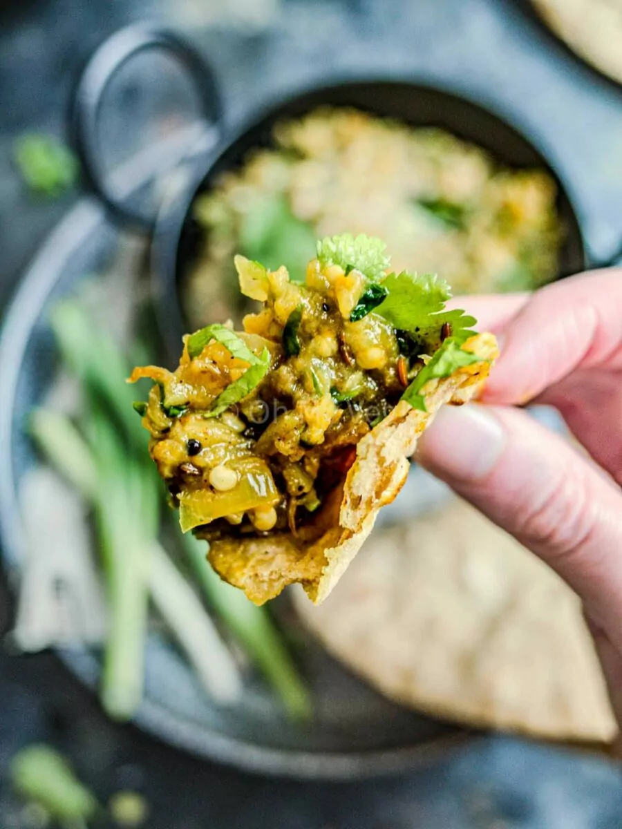 A hand holding a piece of chapati with Maharashtrian vangyache bharit on it.