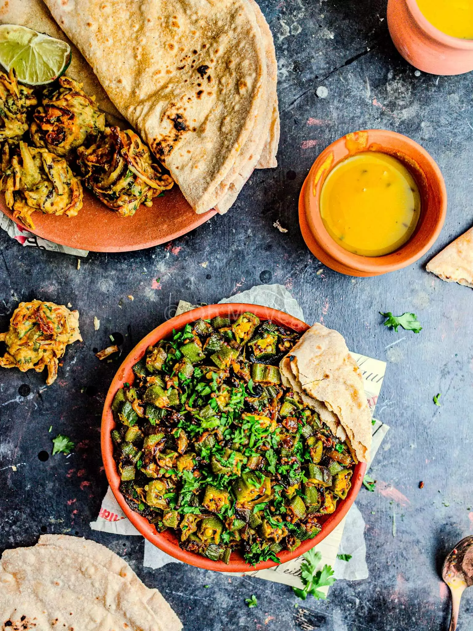Bhindi masala in a clay bowl with dal and onion bhaji.