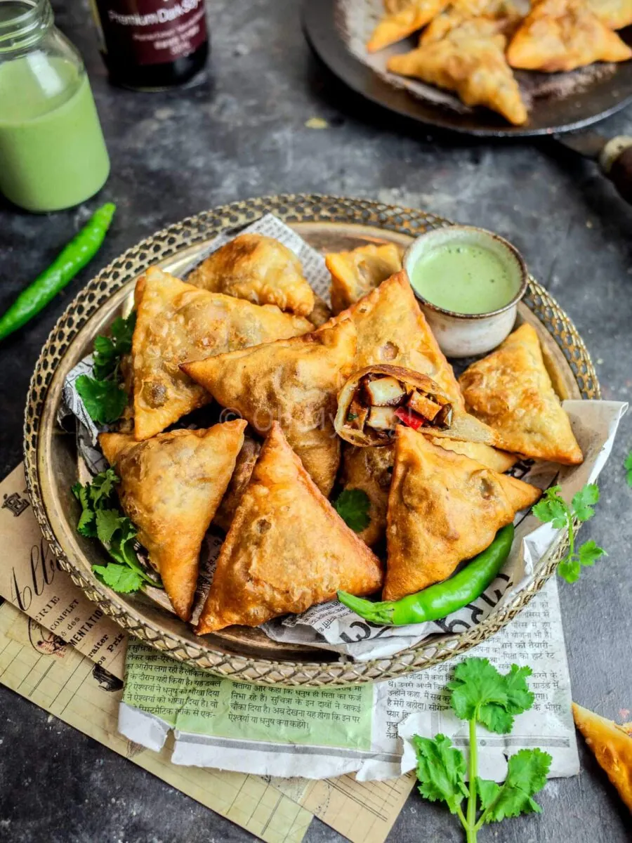 Chilli paneer samosas on a silver platter with chillies and sauce in a small pot.