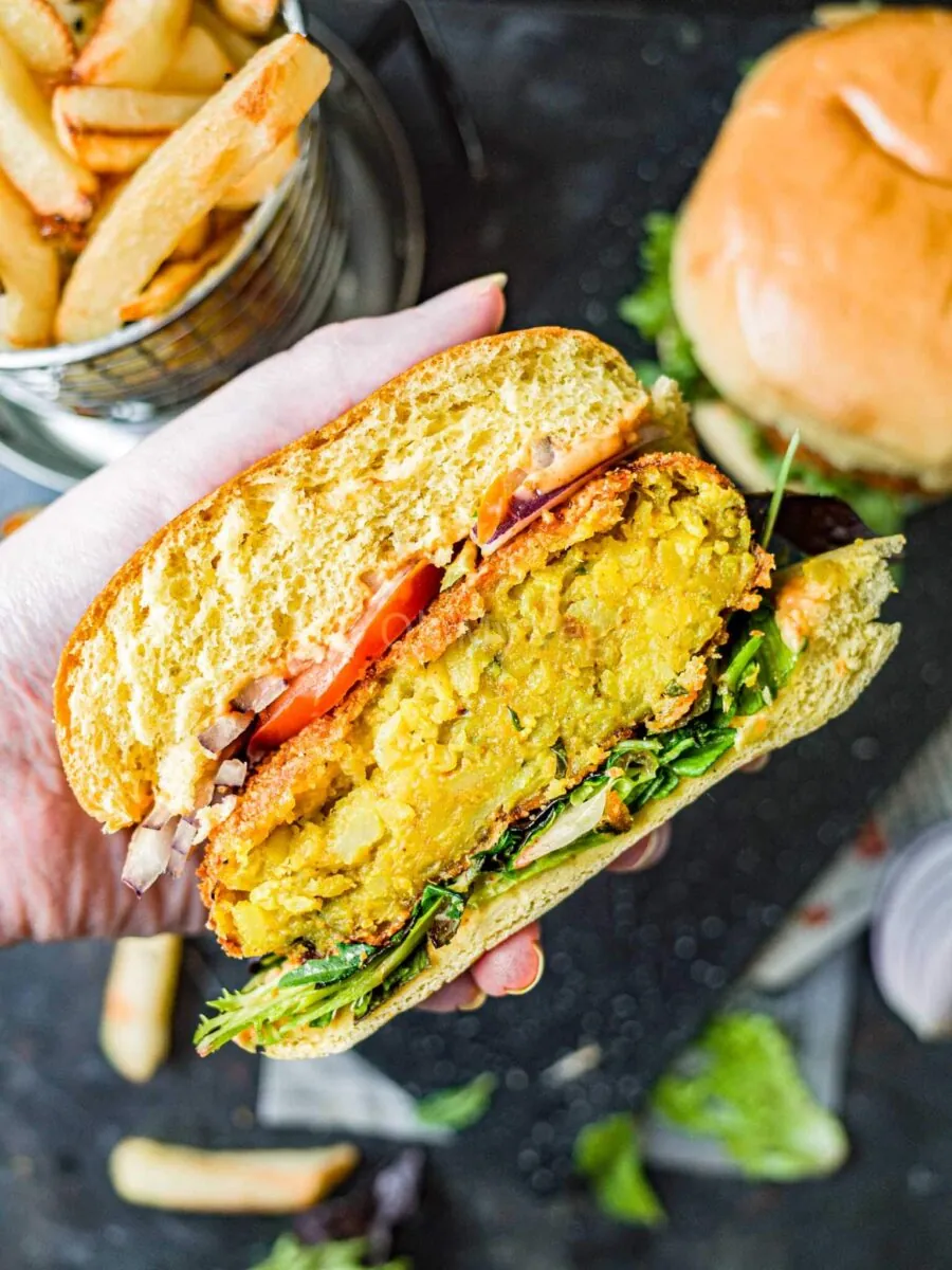 Hand holding an aloo tikki burger cut in half, so you can see inside the burger.