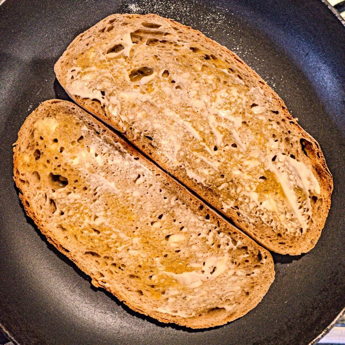 Raw, buttered bread being toasted in a pan.