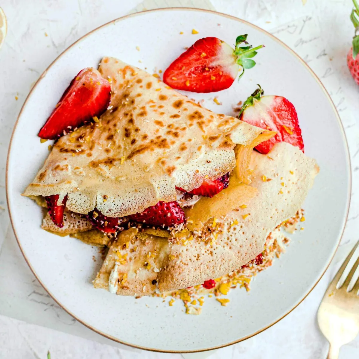 Coconut milk crepes with macerated strawberries on a white plate.