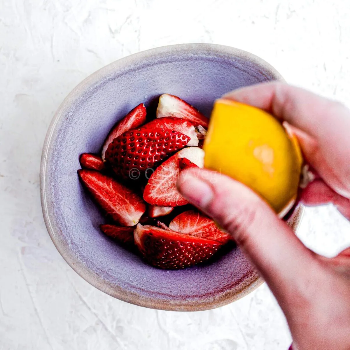 Person squeezing lemon into a bowl of strawberries.