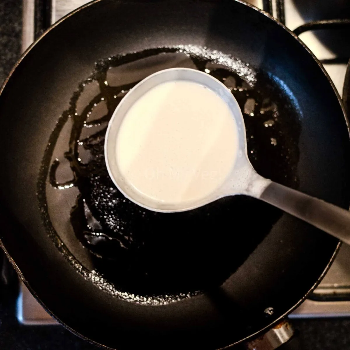 Ladle pouring coconut milk crepe batter into a pan.