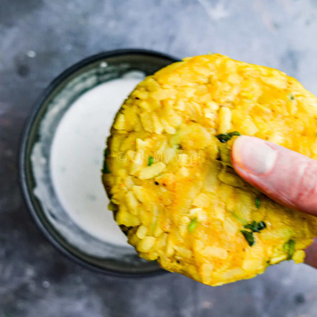Hand dipping aloo tikki in batter.