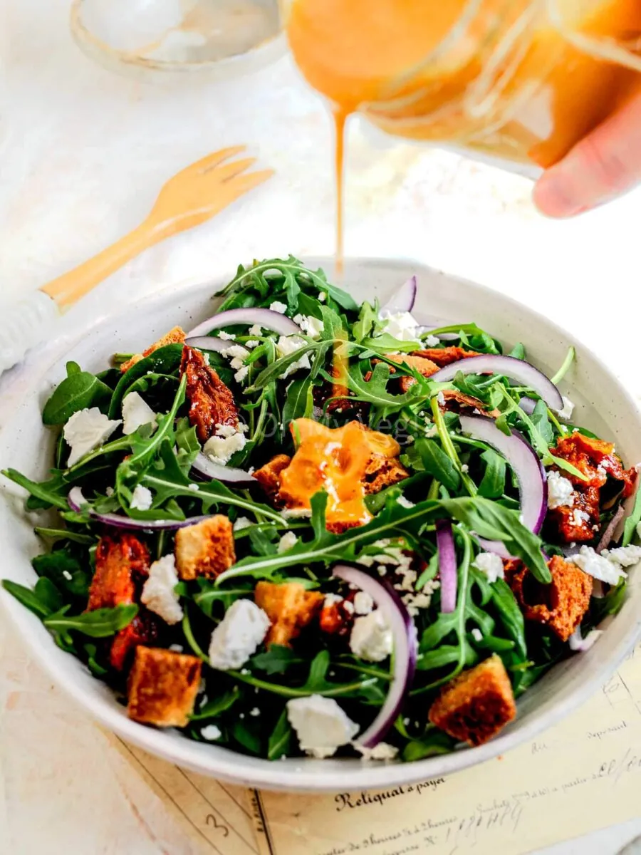 Pouring sundried tomato dressing onto spinach and arugula salad.
